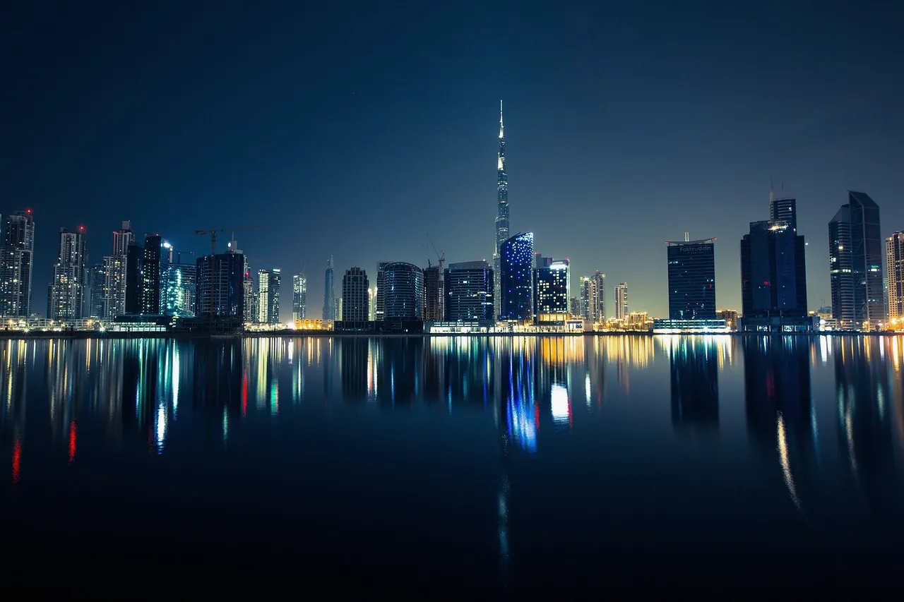 The Dubai skyline at night with the Burj Khalifa at centre, towers reflected in dark still water.