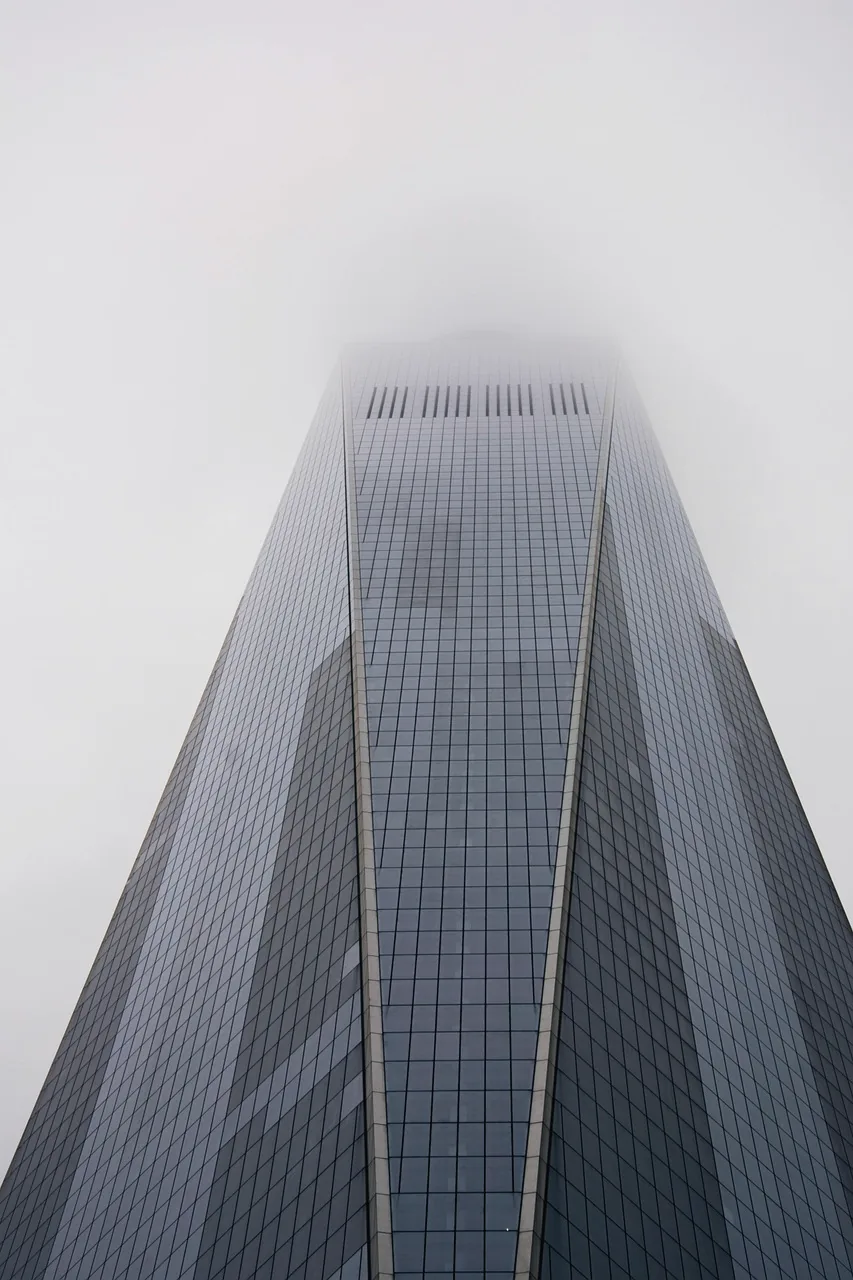 Looking up a glass skyscraper whose top disappears into white fog.