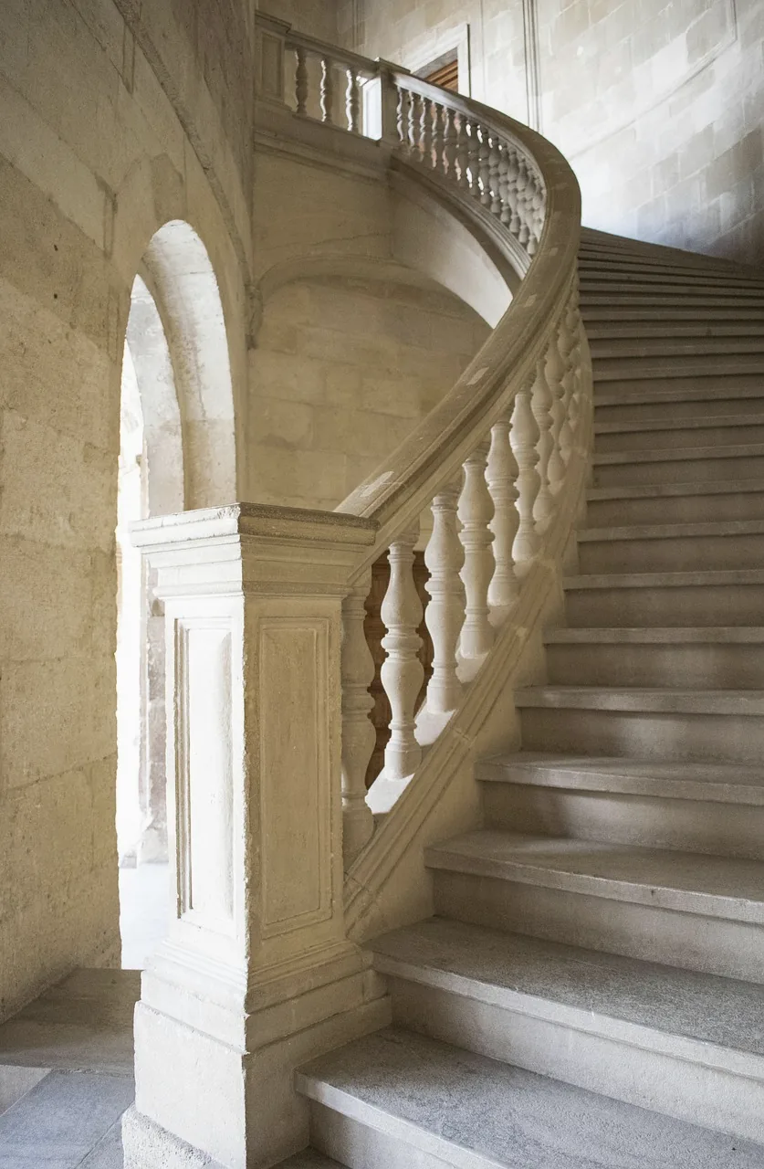 A carved limestone staircase with a balustrade curving upward inside the Palace of Charles V in Granada.