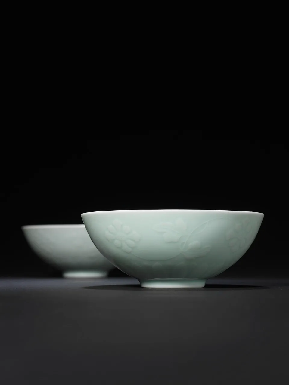 Two pale celadon porcelain bowls on a dark surface against a black background.