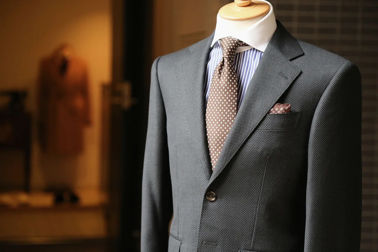 A grey tailored suit jacket with patterned tie and pocket square on a mannequin in a tailor's shop.